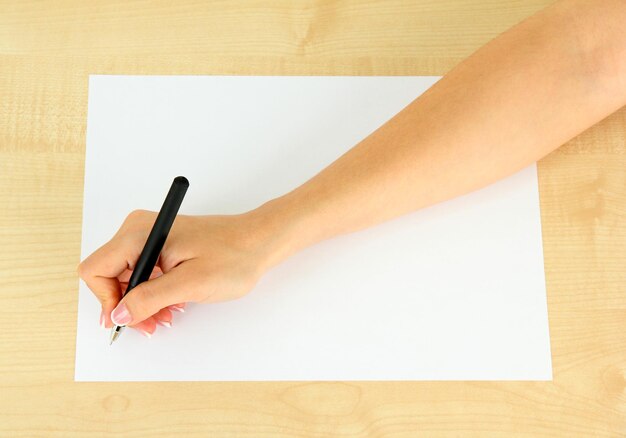 Ręka z długopisem na białym papierze na drewnianym tle