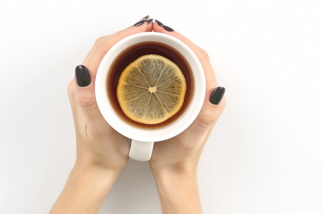 Ręka z filiżanką herbaty z cytryną na białym blacie