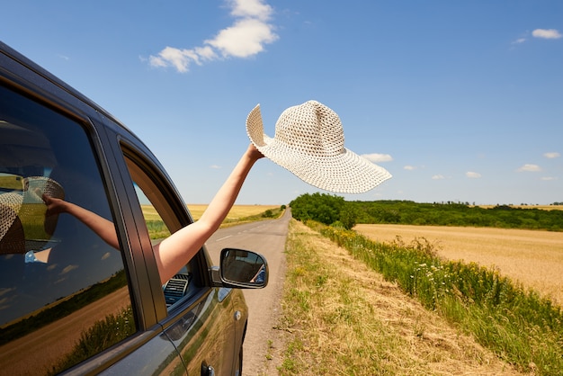 Ręka z kapeluszem z okna samochodu na drodze.