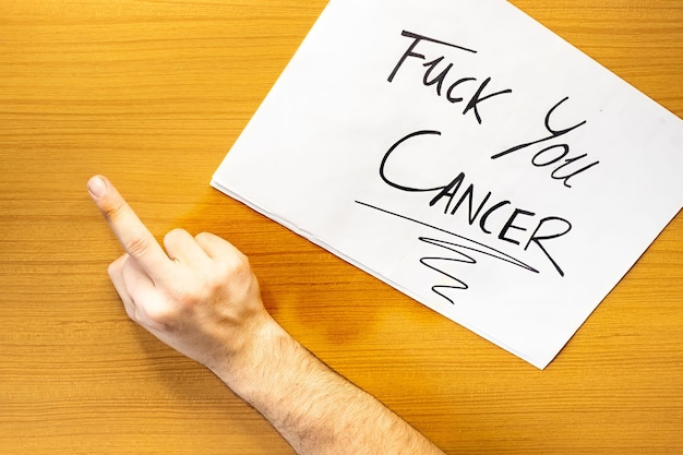 Ręka z kartą na stole FUCK CANCER Wiadomość na kartonie przeciwko rakowi Koncepcja ręcznego pisania na kartonie FUCK CANCER