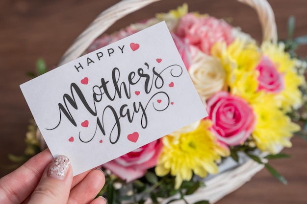 Ręka z kartką z życzeniami na dzień matki Piękne kwitnące kwiaty w koszykuKreatywny bukiet z chryzantemami róże goździkiprezent kwiatowy
