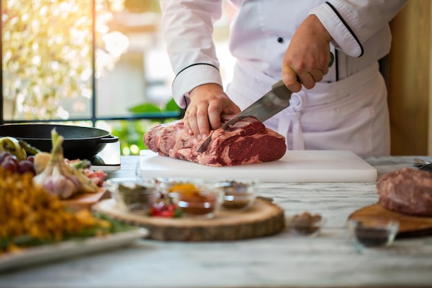 Ręka z nożem tnie mięso. Deska do gotowania na szarym stole. Polędwica wołowa na stek. Szef kuchni pracuje w restauracji.