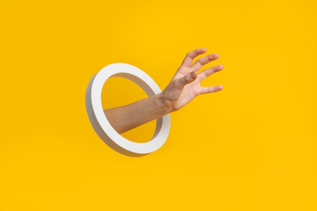 Ręka z okrągłym otworem podnosi niewidzialny przedmiot na żółtym tle/