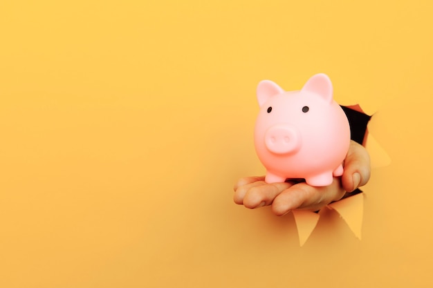 Ręka z piggy bank przez żółtą papierową dziurę koncepcji finansowej i biznesowej