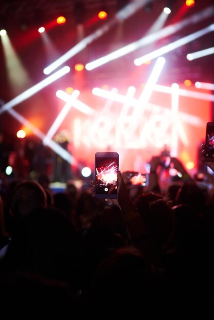 Ręka z telefonem nagrywa festiwal muzyczny na żywo Ludzie robią zdjęcia telefonem podczas koncertu