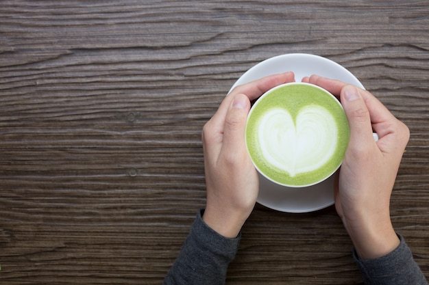 Ręka z zielonej herbaty latte na drewnianym tle