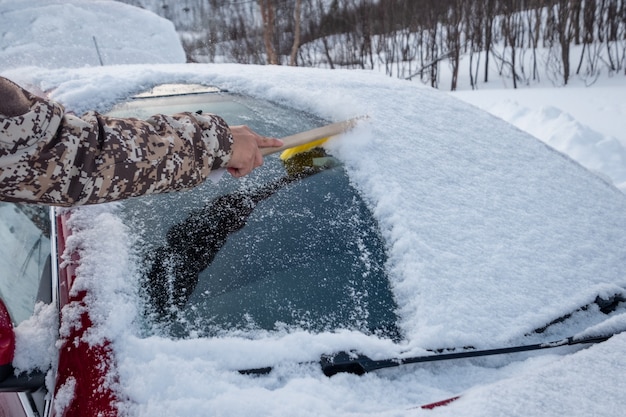 Ręka za pomocą szczotki zamiata śnieg na przedniej szybie samochodu w zimie