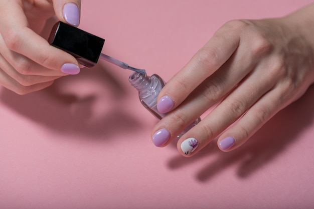 Ręki kobieta na różowym tle z purpur manicurem i otwartą butelką gwóźdź
