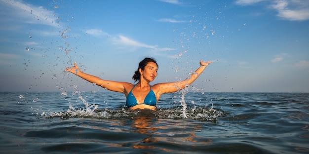 Relaks i zdrowy tryb życia. Młoda piękna i emocjonalna kobieta pływa w morzu w słoneczny dzień
