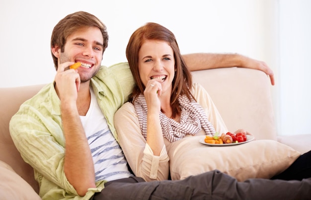 Relaks przy dobrym jedzeniu i lepszym towarzystwie. Młoda para relaksuje się na kanapie ze zdrową przekąską.