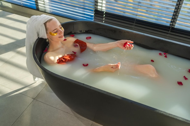 Relaks w spa kobieta leżąca w wannie z czerwonymi różami płatkami dziewczyna relaksująca się w łazience w domu ładnie