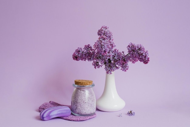 Relaksujący zestaw spa z aromatem bzu Naturalnie mydlana sól morska i kwiaty w białym wazonie na fioletowym tle