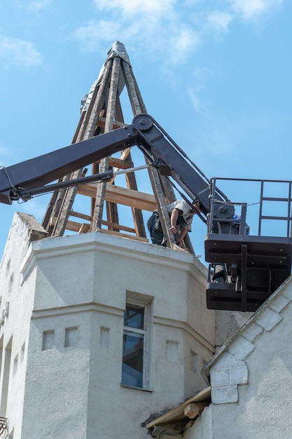 Remont starego drewnianego dachu pięknego zabytkowego budynku Żuraw podnosi budowniczych na wysokość na specjalnej kołysce lub koszu do wykonania pracy Stolarz na dachu