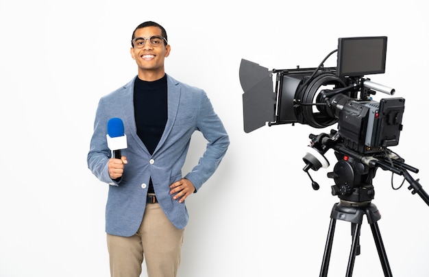 Reporter Afroamerykanin mężczyzna trzymający mikrofon i przekazujący wiadomości na temat izolowanych białych pozowanie z rękami na biodrze i uśmiechnięty