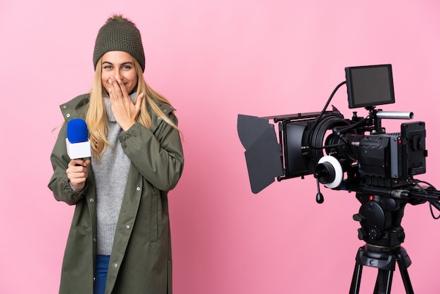 Reporter kobieta trzyma mikrofon i donosi wiadomości nad odosobnionym różowym szczęśliwym i uśmiechniętym nakrywkowym usta z ręką