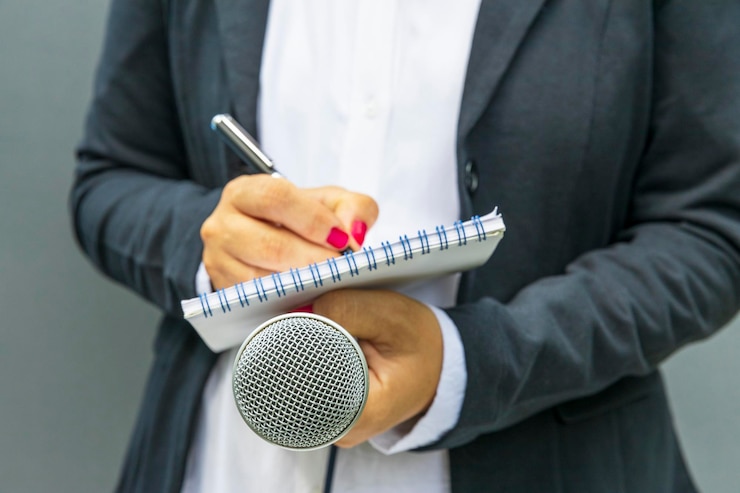 Zdjęcie reporterka na konferencji prasowej lub informacyjnej pisząca notatki z mikrofonem w ręku