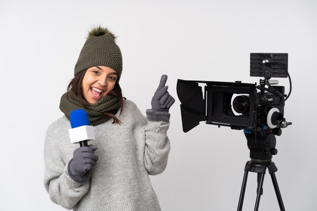 Reporterka trzymająca mikrofon i przekazująca wiadomości nad izolowaną białą ścianą wskazującą palcem na boki i szczęśliwa