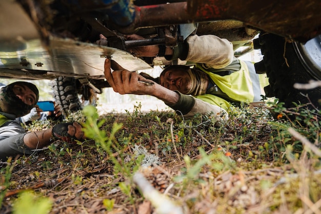 REPUBLIKA KARELII ROSJA OKOŁO CZERWCA 2022 Turniej Offroad Ladoga Trophy 2022 wokół jeziora Ładoga Racer naprawa jeepa SUV leżącego na ziemi pod dnem