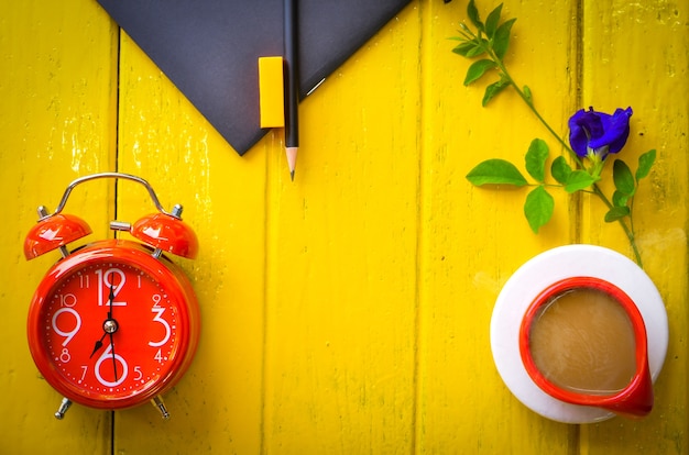 Zdjęcie retro zegar z filiżanką kawy i materiały na żółtym tle, opróżnia przestrzeń.