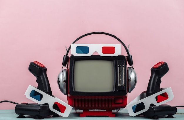 Retrogaming. Konkurs gier wideo. Stary telewizor ze słuchawkami, anaglifowymi okularami 3D i dwoma joystickami na różowym tle. Atrybuty lat 80.