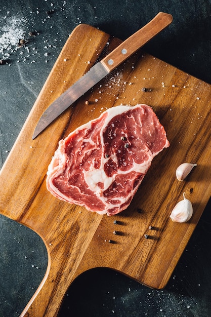 Zdjęcie ribeye steak z drewnianą deską do cięcia na kamiennym czarnym tle