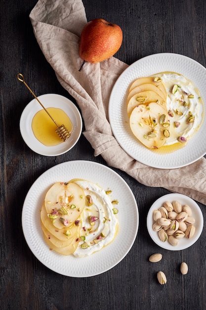 Ricotta z gruszkami, pistacjami i miodem lub syropem klonowym na dwóch białych talerzach na ciemno