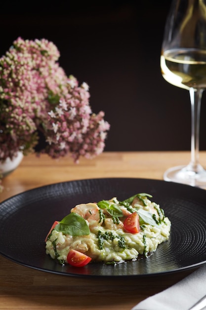 Risotto z pesto bazylią i pomidorkami koktajlowymi zbliżenie w czarnym talerzu na drewnianym stole risotto na drewnianym stole restauracja z lampką wina zdjęcie