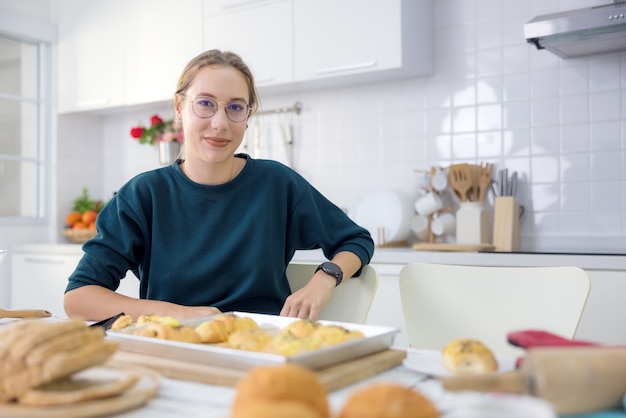 Zdjęcie robienie ciast i ciasteczek to świetna zabawa. w swojej kuchni młoda kobieta trzyma pyszny świeży chleb.