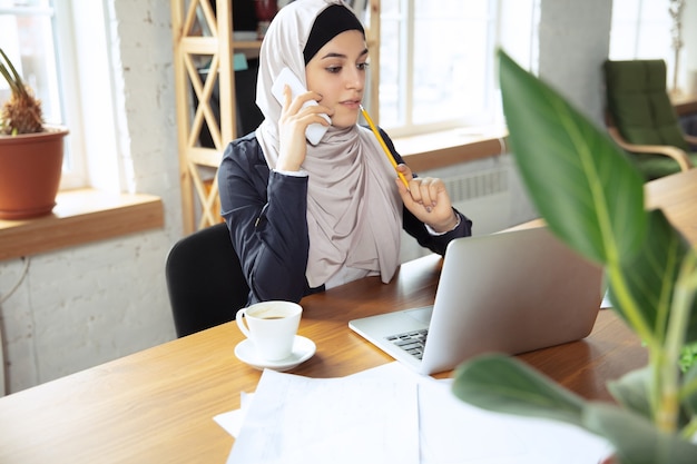 Robienie notatek podczas rozmowy przez telefon. Arabska kobieta nosi hidżab podczas pracy na openspace lub w biurze. Pojęcie zawodu, wolność w biznesie, przywództwo, sukces, nowoczesne rozwiązanie.