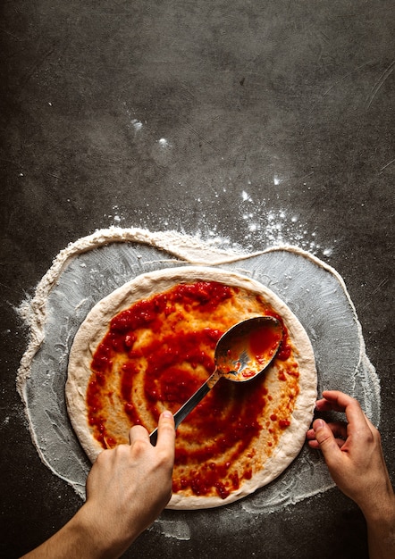 Zdjęcie robienie pizzy rozprowadzając sos pomidorowy na cieście