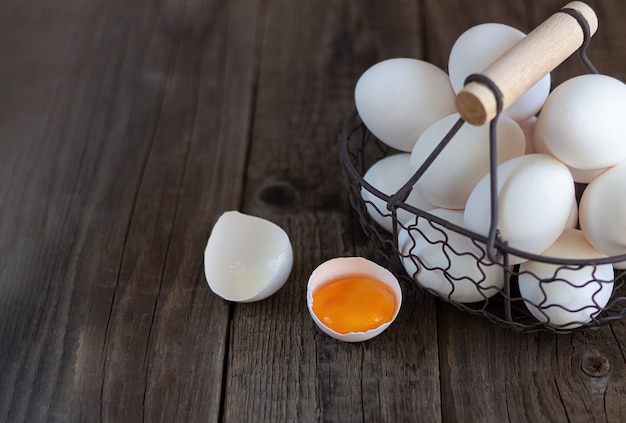 Rocznika metalu kosz surowi jajka obok eggshell z żółtkiem na nieociosanym drewno stole