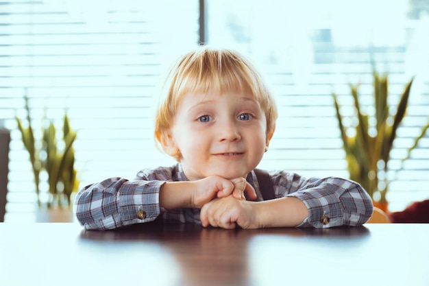 Roczny chłopiec z blond włosami w koszuli uśmiecha się szczęśliwe dziecko na stole
