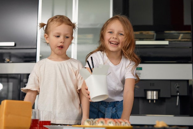 Rodzeństwo Dwóch Małych Dziewczynek Bawi Się I Je W Kuchni W Domu Z Japońskim Jedzeniem
