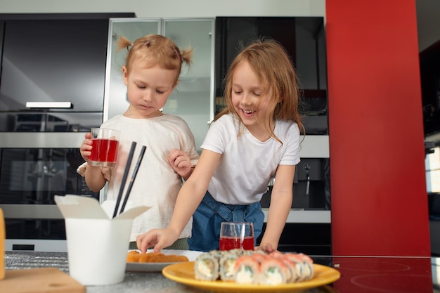Rodzeństwo dwóch małych dziewczynek bawi się i je w kuchni w domu z japońskim jedzeniem