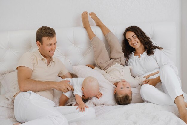 Rodzice bawiący się z dziećmi w łóżku w przytulnym białym mieszkaniu
