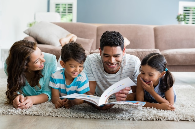 Rodzice i dzieci leżące na dywanie i czytające książkę w salonie