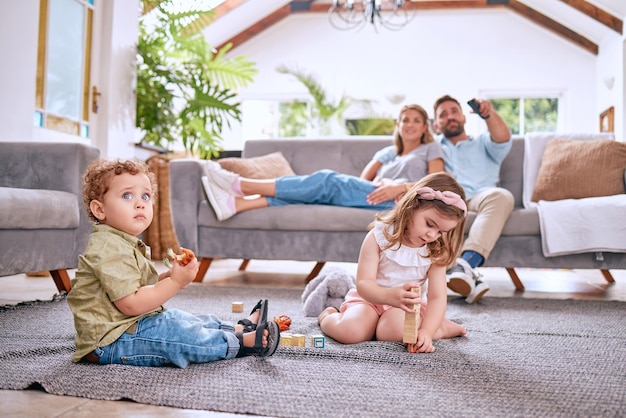 Rodzice na kanapie dzieci bawią się na podłodze w domu i razem w czasie rodzinnym w weekendowy poranek w Dallas Streaming filmu małe dzieci łączą się z zabawkami, a tata szuka kanału oglądającego telewizję z mamą