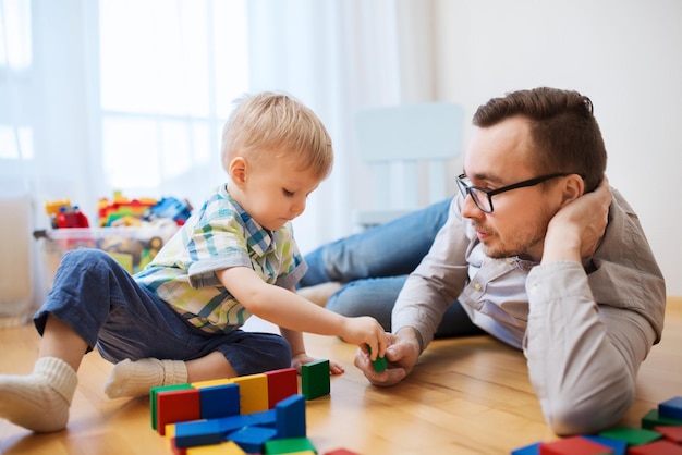 rodzina, dzieciństwo, kreatywność, aktywność i koncepcja ludzi - szczęśliwy ojciec i mały syn bawiący się klockami zabawek w domu