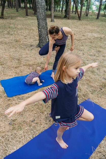 Zdjęcie rodzina fitness i joga szczęśliwa mama ćwiczy z dziewczynkami na trawiastym terenie przeciwko drzewom w