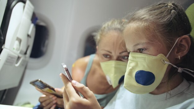 Rodzina kobieta i dziecko dziecko podróżują turystyczny kaukaski w samolocie samolot z noszeniem ochronnej maski medycznej Użyj smartfona mobilnego Zdrowie wirus chroń koronawirusa epidemia sarscov2 covid19