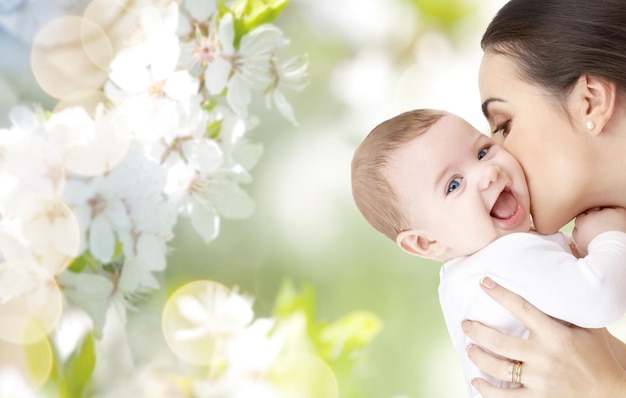 rodzina, macierzyństwo, rodzicielstwo, ludzie i koncepcja opieki nad dzieckiem - szczęśliwa matka całuje urocze dziecko na zielonym naturalnym tle