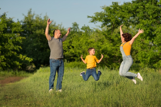 Rodzina: matka, ojciec, syn skaczą z podniesionymi rękami na zielonym polu w lecie