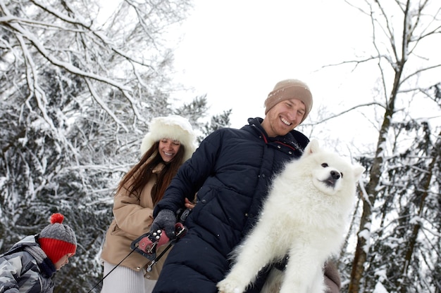 Rodzina matki, ojca i syna bawi się w śnieżnym zimowym drewnie z wesołym psem domowym