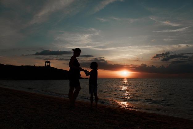 Zdjęcie rodzina na plaży. sylwetki ludzi przed zachodem słońca. 2 osoby trzymające się za ręce