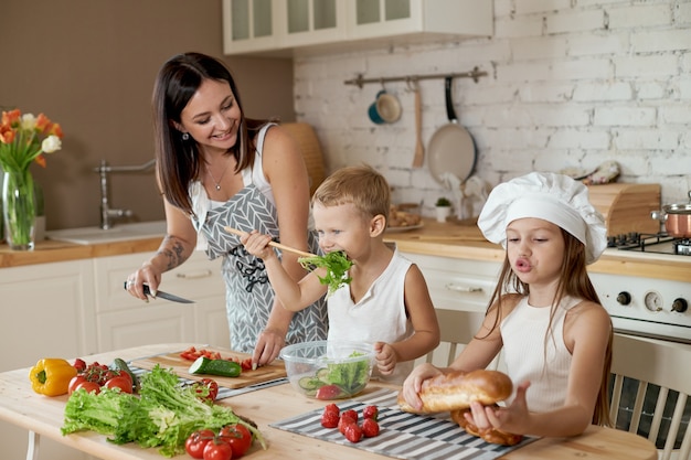 Rodzina przygotowuje obiad w kuchni. Mama uczy swoją córkę i syna przygotowania sałatki ze świeżych warzyw. Zdrowa naturalna żywność, witaminy dla dzieci