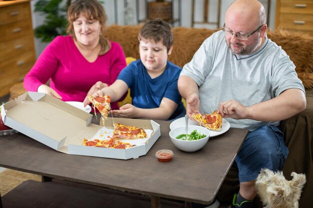 Zdjęcie rodzina rozdaje kawałki pizzy całej rodzinie, a pies czeka na swoją kolej.