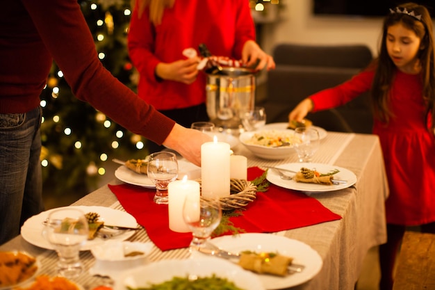 Rodzina świętuje Wigilię Bożego Narodzenia. Serwowany świąteczny stół, z bliska płonące świece. Dziewczyna razem pomaga rodzicom, rodzinie