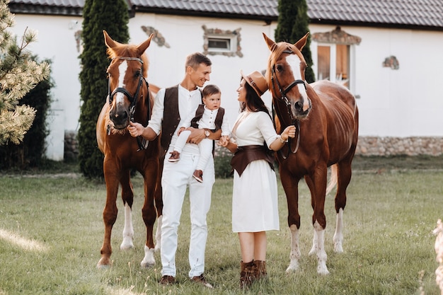 Rodzina W Białych Ubraniach Z Synem Stoi Obok Dwóch Pięknych Koni Na łonie Natury