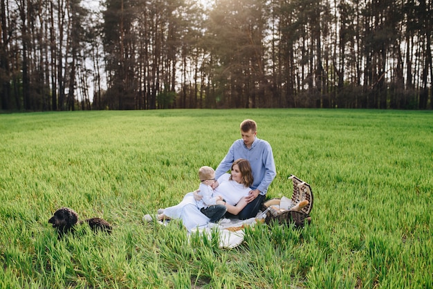 Rodzina w lesie na pikniku. Usiądź na polanie, zielonej trawie. Niebieskie ubrania. Mama i tata bawią się z synem, obejmują się i uśmiechają. Dziecko w okularach.