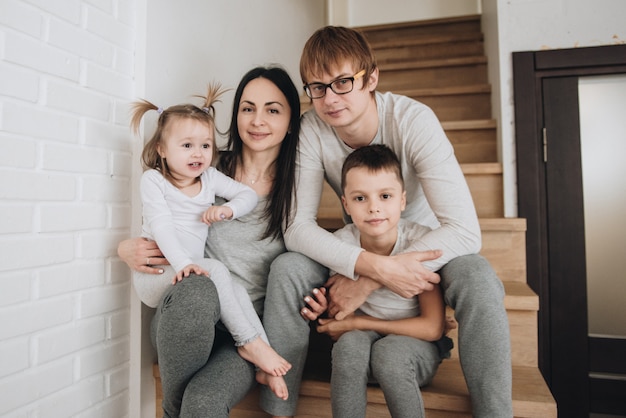 Rodzina w szarej domowej odzieży. W domu na drewnianych schodkach. Duży dom. Mama, tata, syn, córka. Miłość, portret rodzinny.